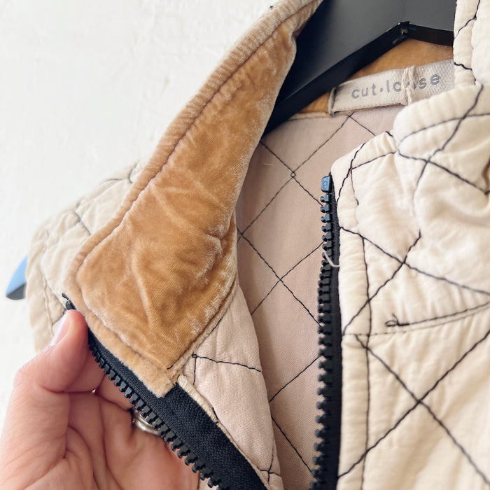 Close-up of the collar of a quilted vest with a hand holding the zipper, brand 'cut loose' visible.