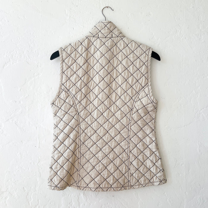 Cream-colored quilted vest with diamond pattern on a hanger against a white wall, viewed from the back