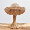 Natural raffia kettle brim hat with wide floppy brim and open block crochet weave, shown on a wicker hat stand — front view