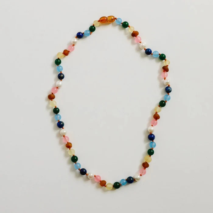 CanyonLeaf Raw Baltic Amber and Pearl + Multi Colored Gemstones Necklace — a hand-knotted necklace alternating raw honey amber, white pearl, pink rose quartz, blue aquamarine, navy lapis, green jade, and yellow amber beads with a honey amber screw clasp, laid flat on a light grey background