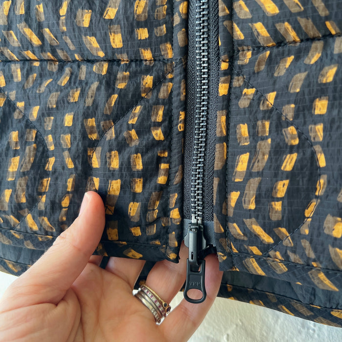 Hand holding a black and gold patterned fabric with a zipper