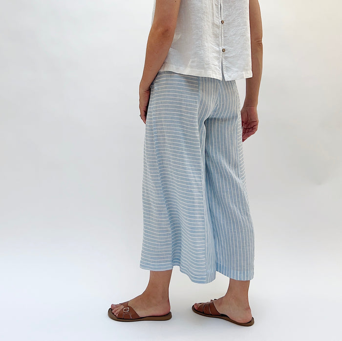 Person wearing light blue striped pants and a white shirt on a white background as seen from behind.