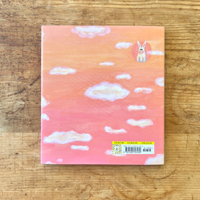 The back cover of the book with a rabbit illustration on a cloud-patterned cover, placed on a wooden surface.