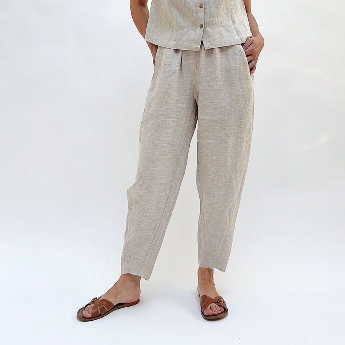 Person with their hands in their pockets wearing beige linen pants and a matching top on a white background.