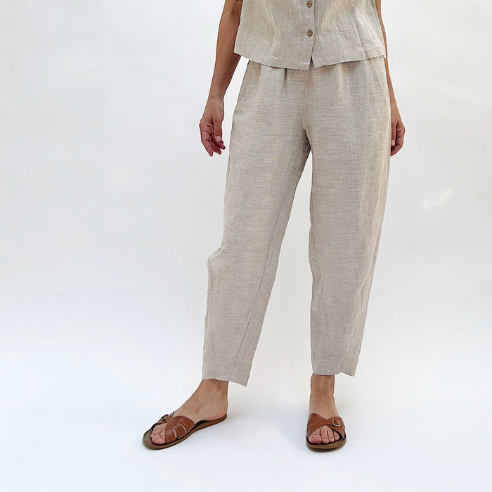 Person with their hands at their sides wearing beige linen pants and a matching top on a white background.