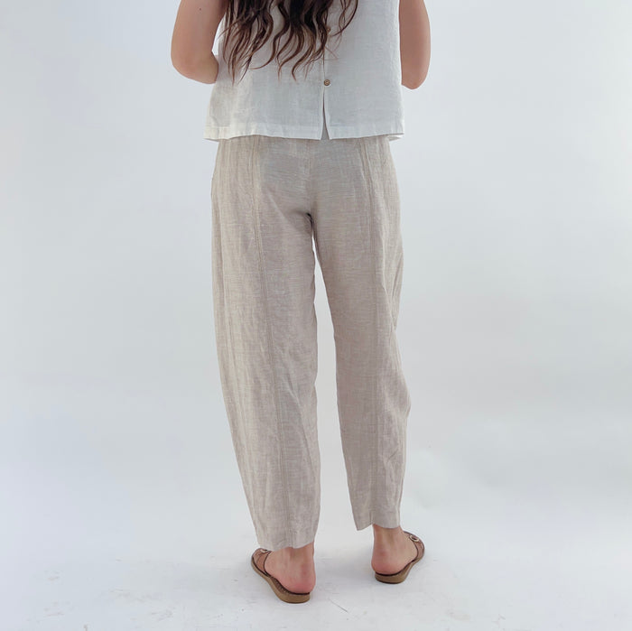 Person wearing beige linen pants and a white linen tank on a white background as seen from behind.