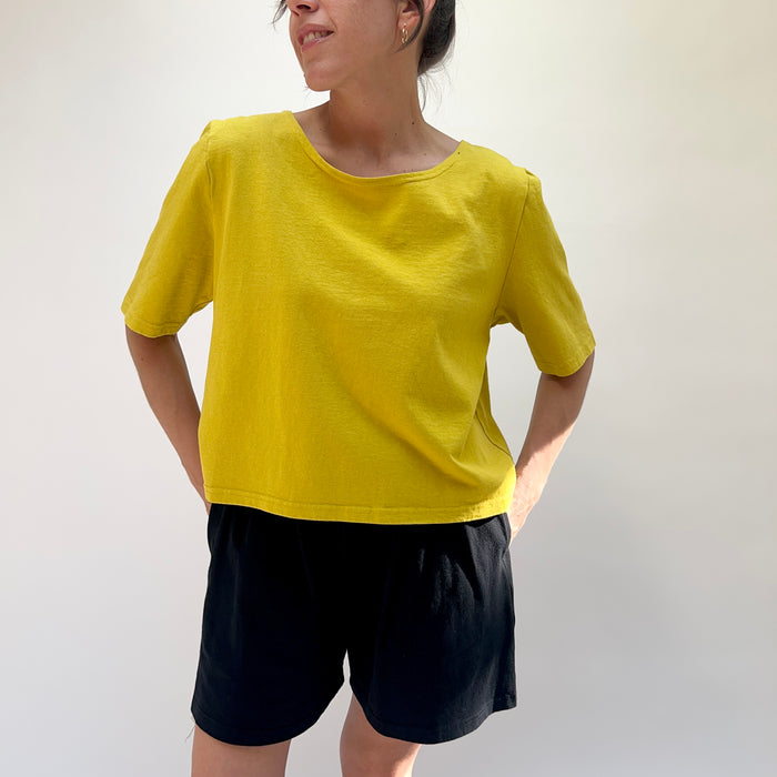 Person wearing a yellow shirt and black shorts against a plain background