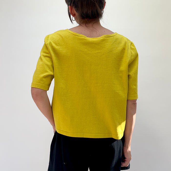Person wearing a yellow top and black pants against a plain background