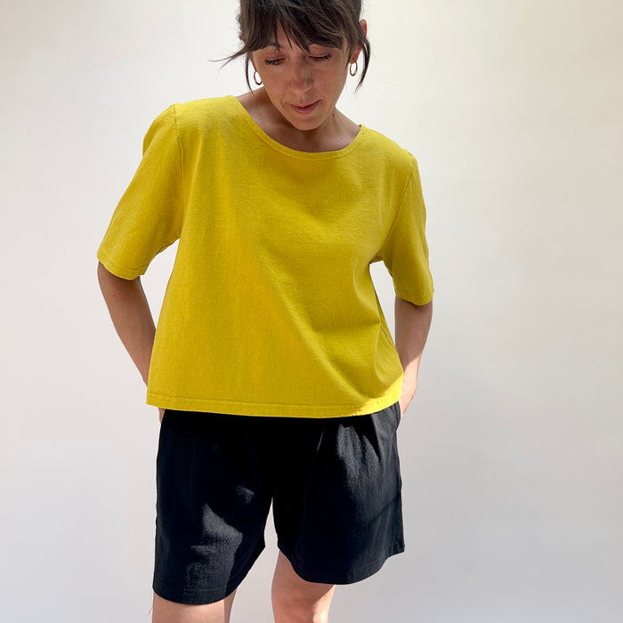 Person wearing a yellow shirt and black shorts against a plain background