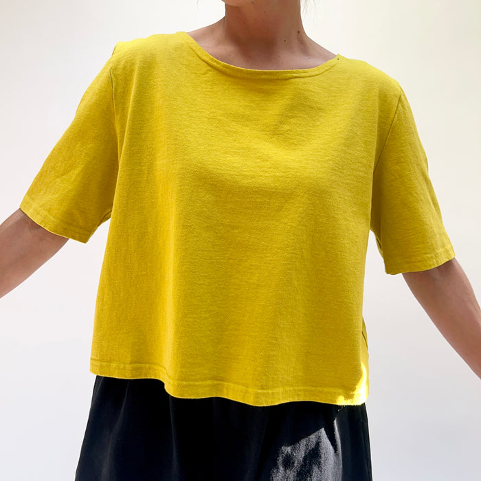 Person wearing a yellow shirt and dark pants against a white background