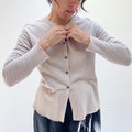 A person wearing a beige crop cardigan with long sleeves, snap buttoned front, and a round neckline.