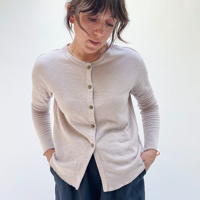 A person wearing a beige crop cardigan with long sleeves, snap buttoned front, and a round neckline.