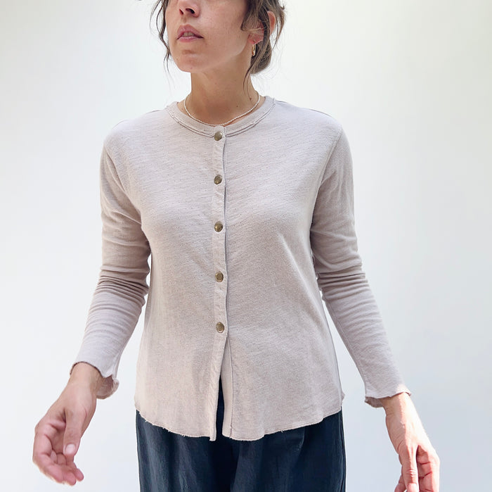 A person wearing a beige crop cardigan with long sleeves, snap buttoned front, and a round neckline.