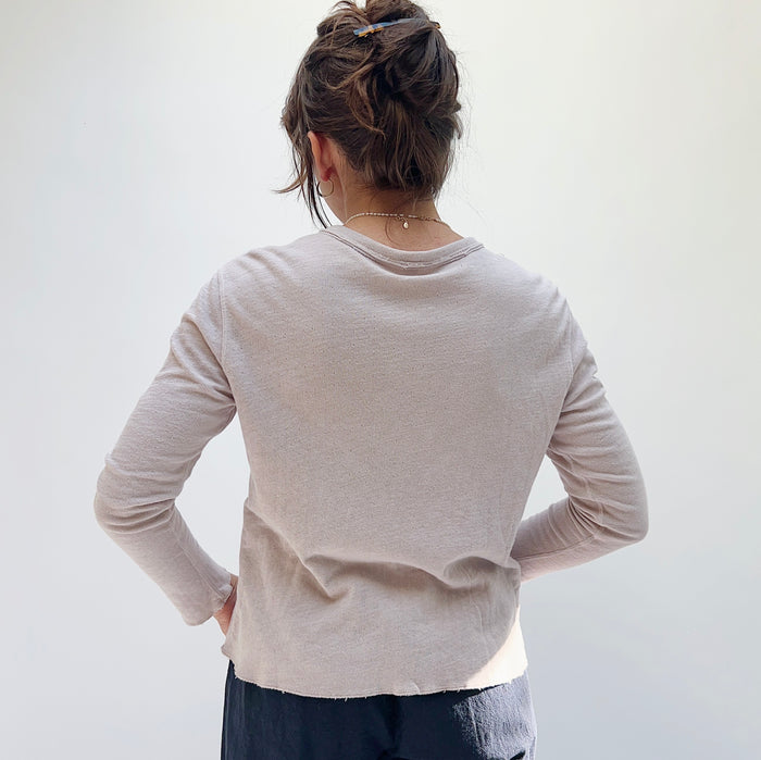A person wearing a beige crop cardigan with long sleeves, snap buttoned front, and a round neckline, viewed from behind.