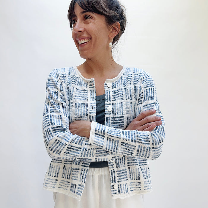 Woman smiling with arms crossed wearing the Softly Stamped Cardigan in White, featuring a navy brushstroke print and pearlized buttons, layered over a dark tank and white skirt