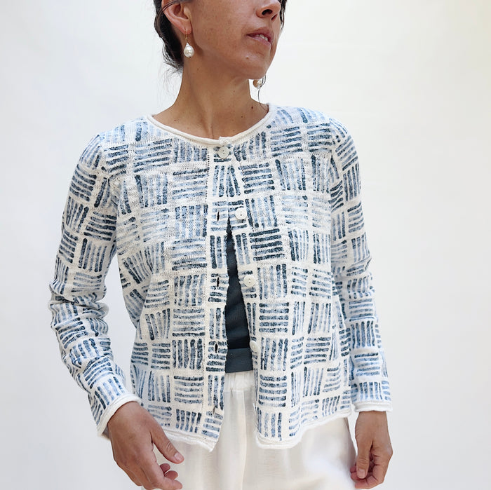 Front view of the Softly Stamped Cardigan in White worn open, showing pearlized button placket, round neckline, and navy stamp print, layered over a dark tank and white trousers
