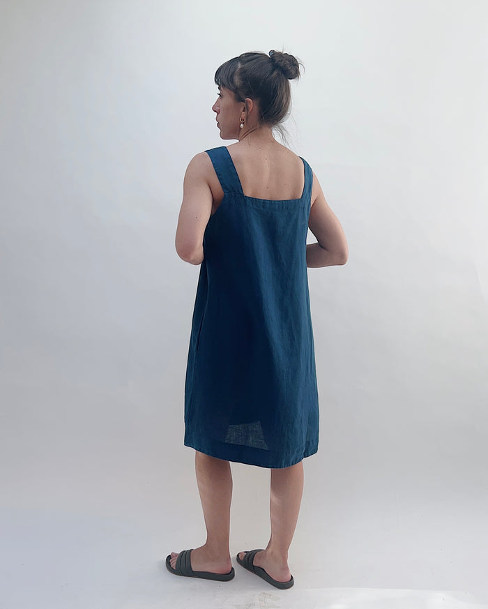 Woman wearing a dark blue dress against a white background, viewed from the back