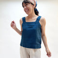 Woman wearing a blue sleeveless top and beige pants against a white background