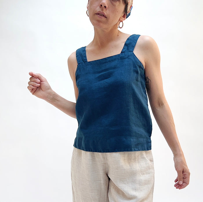 Person wearing a blue sleeveless top and beige pants on a white background