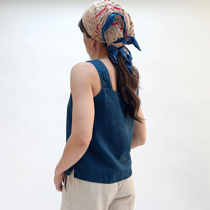 Person wearing a blue sleeveless top and patterned headscarf on a white background, viewed from the back