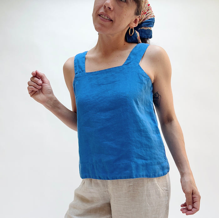 Person wearing a blue tank top and beige pants against a white background