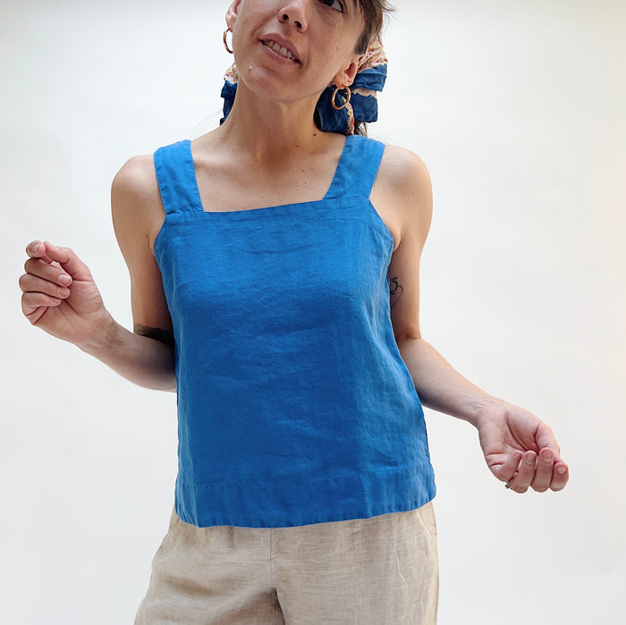 Person wearing a blue tank top and beige pants on a white background