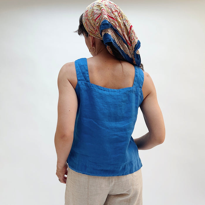Person wearing a blue sleeveless top and patterned headscarf on a plain background, viewed from the back