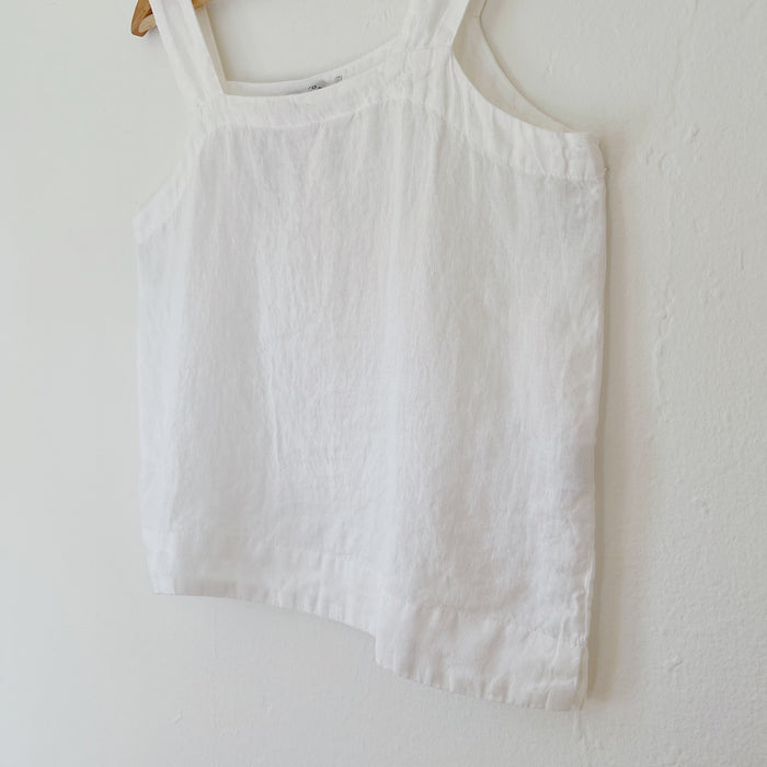 White tank top hanging on a wooden hanger against a white wall.