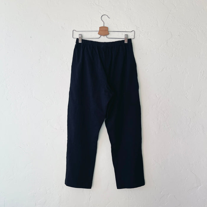 A pair of black cotton pants hanging on a hanger against a white wall.
