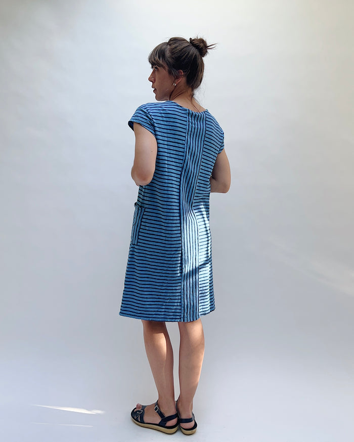 Woman wearing a dark-blue and light-blue striped dress against a white background, viewed from behind