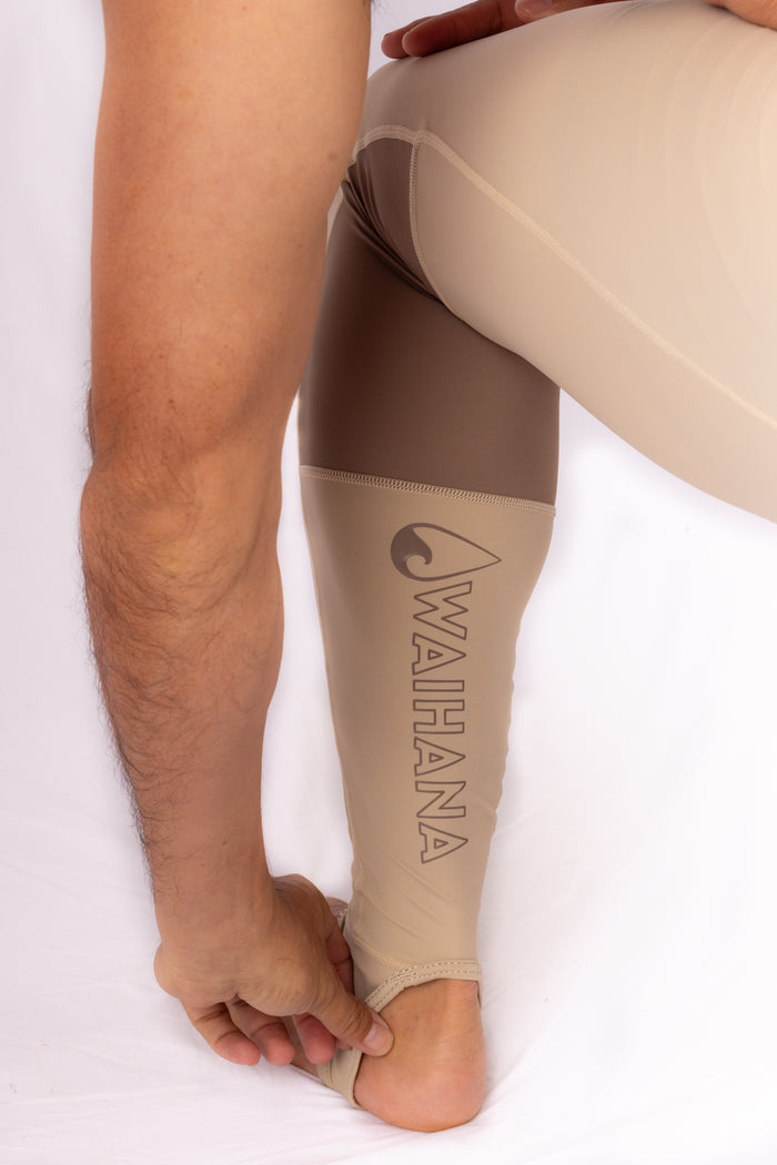 Man wearing Waihana Tan Carvico Lycra leggings with a brown and tan color-block pattern and Waihana logo printed on the lower leg, shown against a white studio background.