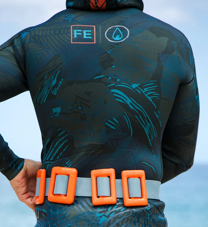 Rear view of a male model wearing a dark teal tropical-print hooded wetsuit with Waihana and FE logos, fitted with an orange Thunderstorm dive weight belt holding grey lead weights.