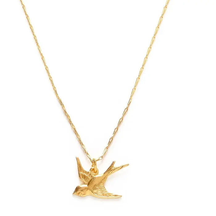 Close-up of a gold necklace with small gold charm in the shape of a bird