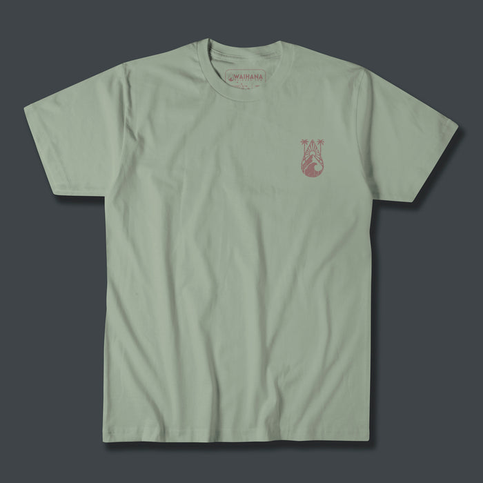 Waihana Tropic Drop Premium Pima T-Shirt in Coastal Sage green with a small pink tropical palm and wave graphic on the left chest, shown flat against a dark gray background.