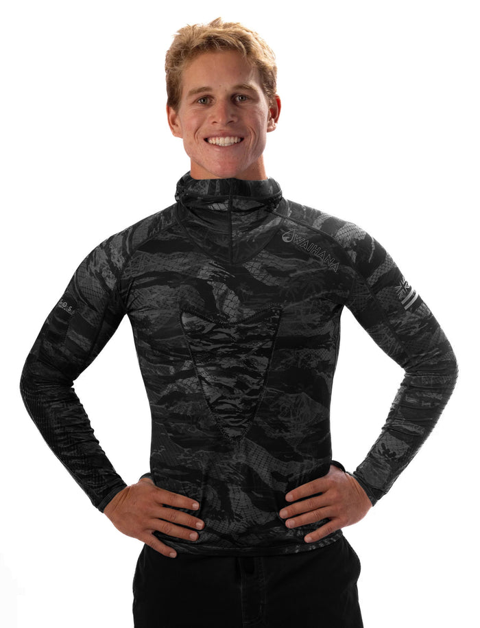 Smiling male model wearing the Waihana Tropicam Black Rashguard in Tactical Black camouflage pattern with integrated hood, hands on hips against a white studio background.
