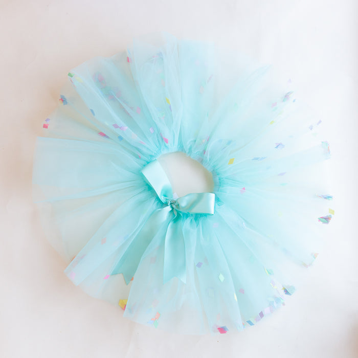 A turquoise tutu with multi-color confetti sprinkled on it, with an elastic waistband and a ribbon tie in the front.