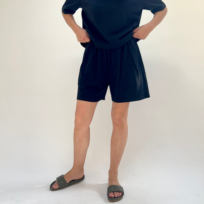Person wearing black shorts and a dark top on a white background