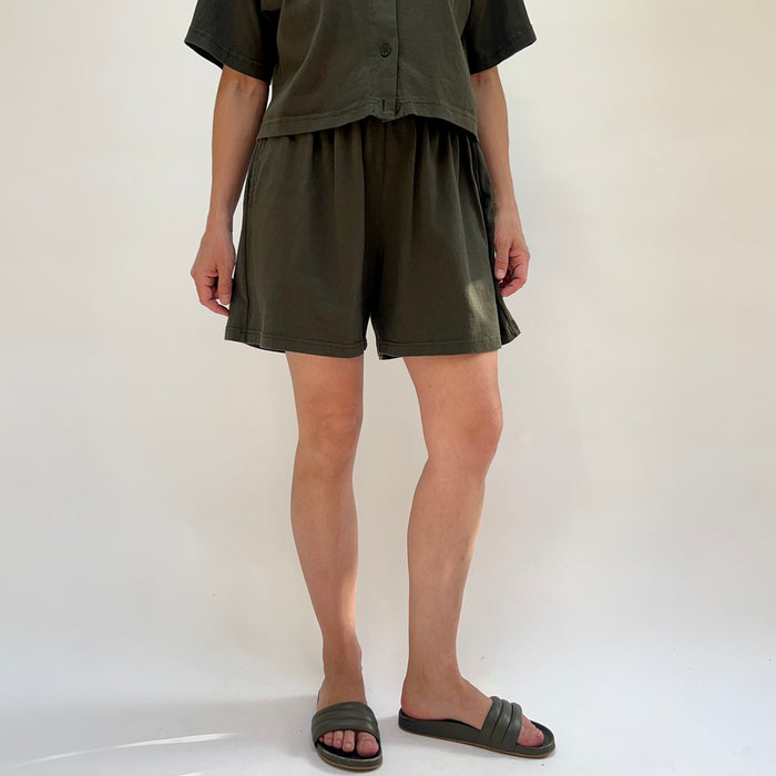 Person wearing olive green shorts and a shirt on a white background