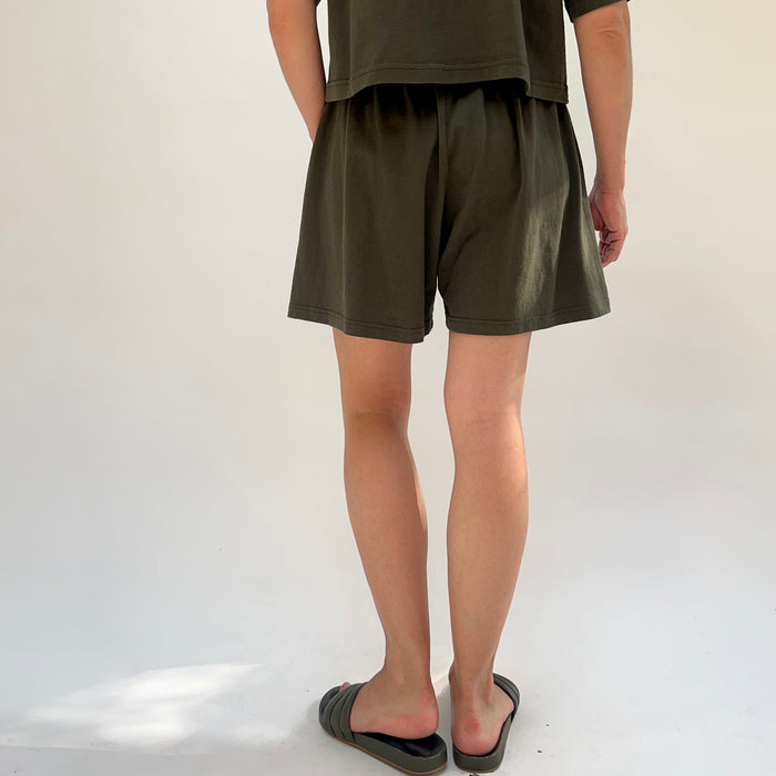 Person wearing olive green shorts and a tank top on a white background, viewed from the back